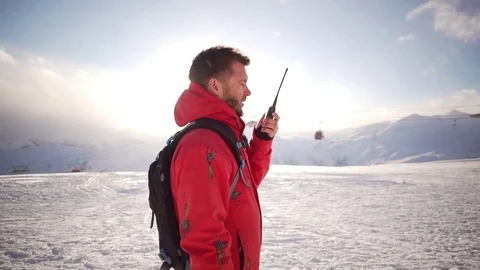 Caucasian male with beard and red parka standing talking on radio on ski Stock Footage