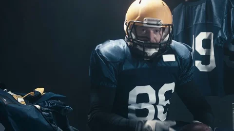 Caucasian male football player sits in the locker room, pointing into camera Stock Footage