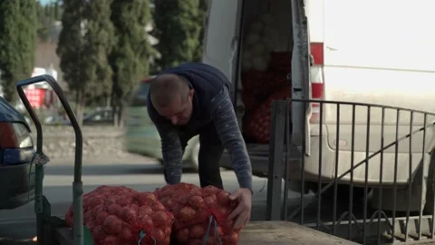 A Caucasian male loader is loading large bags of onions onto a cart. Stock Footage 148611423