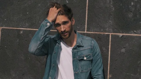 Caucasian male model posing in front of a wall styling his hair Stock Footage 87261141