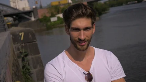 Caucasian male model posing next to river styling and touching his hair Stock Footage 87261098