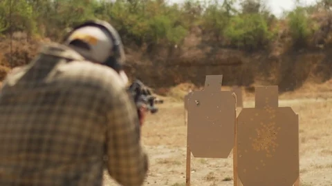 Caucasian male in plaid shirt with headphones shooting at targets with airsoft Stock Footage