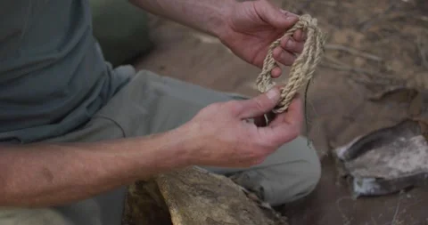 Caucasian male survivalist preparing tinder from twine to make fire at camp in Stock Footage 336482953