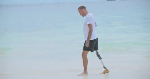 Caucasian man with artificial bionic legs walking along the beach in summer.  Video stock 242443548