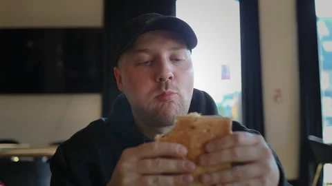 Caucasian man in baseball cap biting a delicious big sandwich.Close up of a man  Stock Footage 340343467