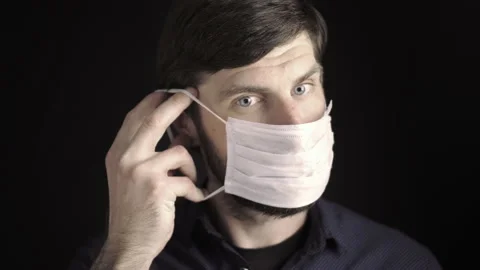Caucasian man with a beard puts on a disposable medical mask, straighten the Stock Footage 139662938