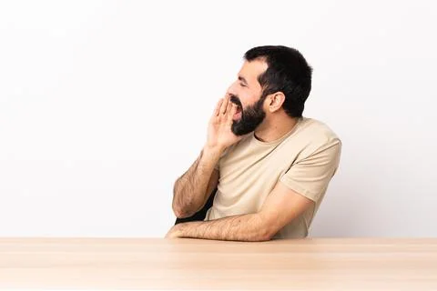Caucasian man with beard in a table shouting with mouth wide open to the side Photos