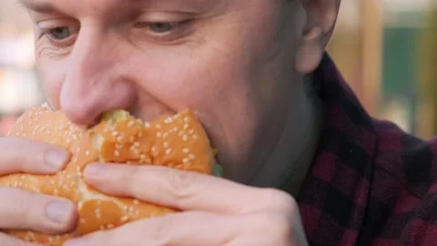 Caucasian man bites an appetizing burger in fast food restaurant Stock Footage 236632909