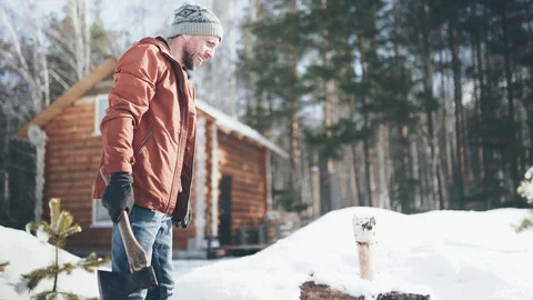 A Caucasian man in a brown jacket, hat, jeans and boots, holding an axe Stock Footage 128004674