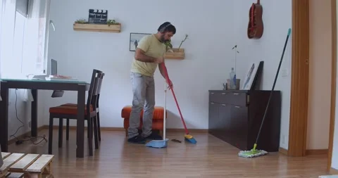 Caucasian man dancing while sweeping his apartment. Man and housework Stock Footage 166123623