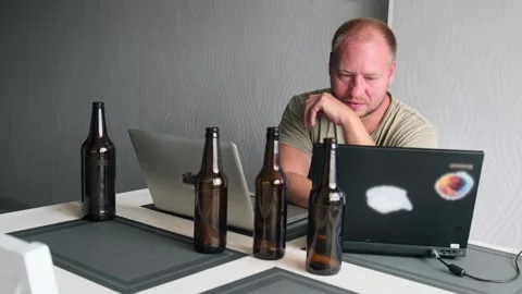 Caucasian man in desk typing on laptops at home next to empty alcohol bottles. Stock Footage 245186529