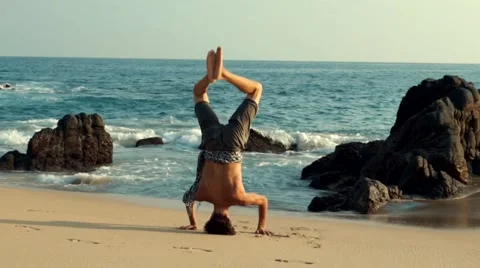 Caucasian man doing head stand on the beach Stock Footage 61955371