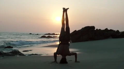 Caucasian man doing head stand on the beach at sunset Stock Footage 61955474