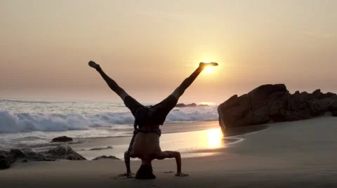 Caucasian man doing head stand on the beach at sunset Stock Footage 61955519