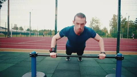 Caucasian man doing push-up exercises on a rack, exercising on an outdoor Stock Footage 149750098