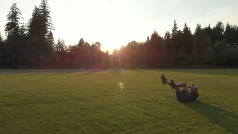 Caucasian man doing sit ups in a field at sunset. 4K 24FPS. Stock Footage 140951915