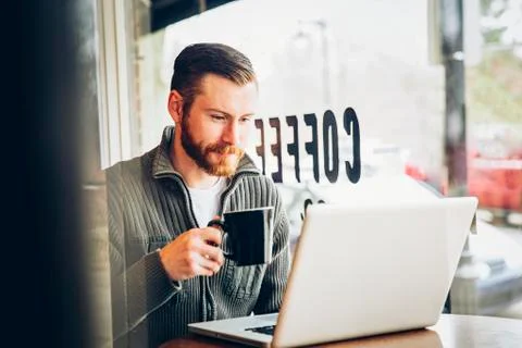 Caucasian man drinking coffee and using laptop in cafe Stock Photos