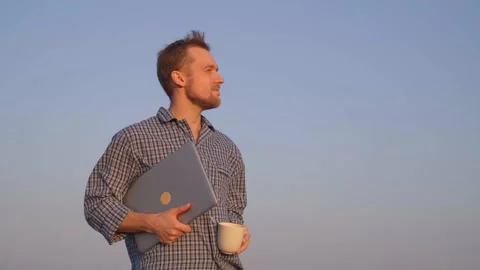 Caucasian man drinking coffee or tea outdoor in nightwear holding laptop, 4K Stock Footage 228675952