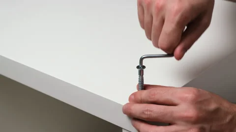 Caucasian man drives hex socket screw with manual hex key into white wooden Stock Footage 163269827