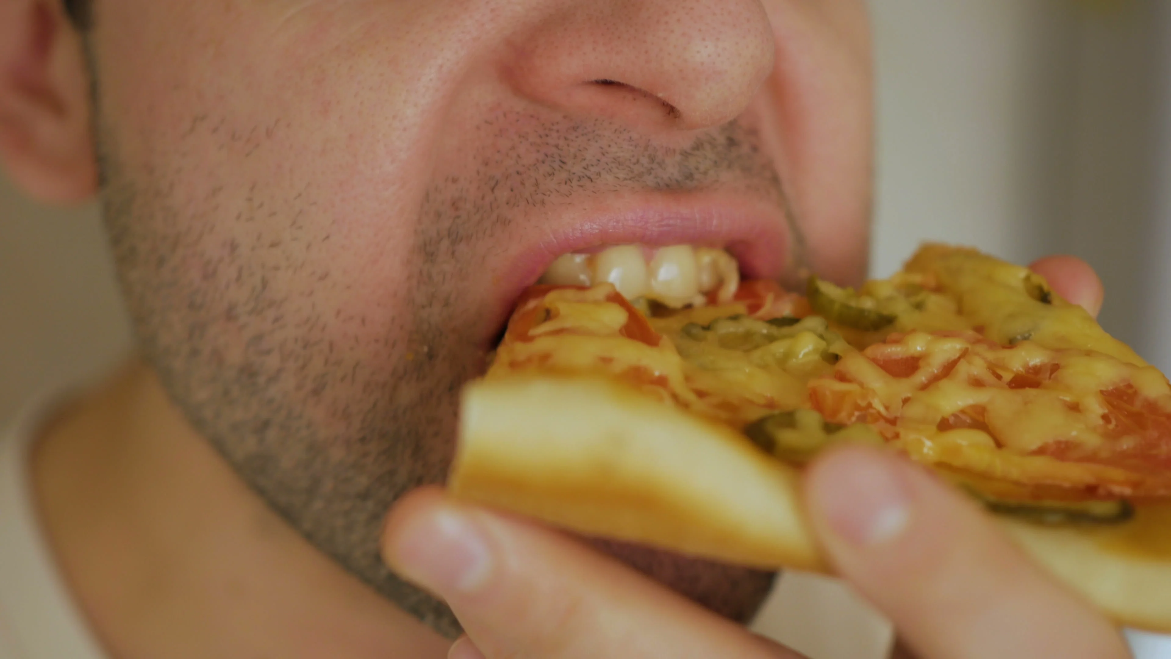 Caucasian man eating pizza. Hungry male taking a bite from pizza. Closeup.