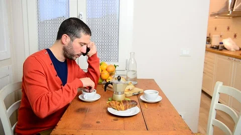 Caucasian man eats alone croissant for breakfast and talks to smartphone 스톡 동영상 122290791