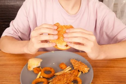 Caucasian man eats half-eaten hamburger, potato chips, onion rings chicken wing Stock Photos