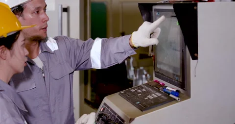 Caucasian man engineer points at CNC display while Asian woman technician checks Stock-Footage 332907395