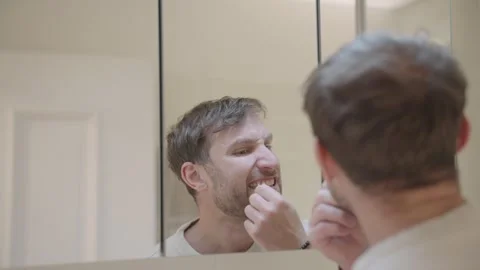Caucasian man flossing his teeth while looking at his reflection in the bathroom Stock Footage 335152291