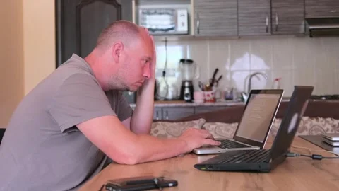 Caucasian man with focused expression in kitchen sitting at laptop. Stock Footage 243580961