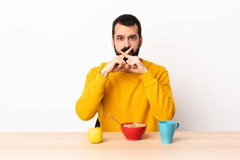 Caucasian man having breakfast in a table showing a sign of silence gesture Stock Photos
