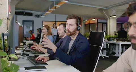 Caucasian man in headset working at computer and talking with client in office Stock Footage 179953445