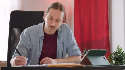 A caucasian man laughs with colleagues while video conferencing from home - slow Stock Footage 129956891