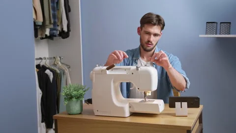 Caucasian man learning how to sew at home watching course on smartphone 스톡 동영상 244801656