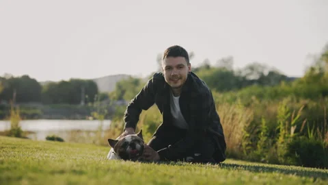 Caucasian Man Lying in a Park, Stroking and Showing Love to His Brooklyn Bulldog Stock Footage 237442697