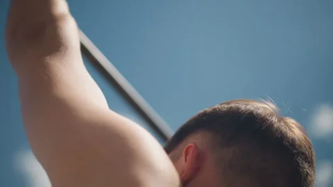 Caucasian man mid pullup, bare torso with engaged back muscles against blue sky Stock Footage 323505369