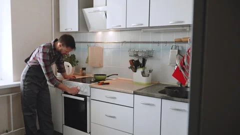 Caucasian man in overalls checks functionality of electric stove in kitchen. Stock Footage 329226538