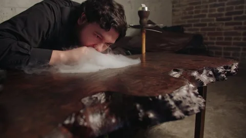 Caucasian man performing hookah smoke experiment in moody lounge Video stock 331883192