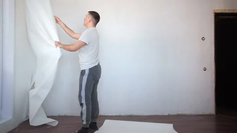 Caucasian man in the process of removing old wallpaper. Male in white t-shirt Stock Footage 171728939