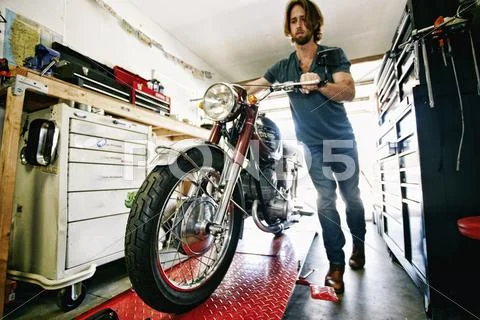 Caucasian Man Pushing Motorcycle On Repair Stand In Garage