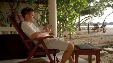 Caucasian man puts down his phone and relaxes in a chair on the beach Video stock 195941632