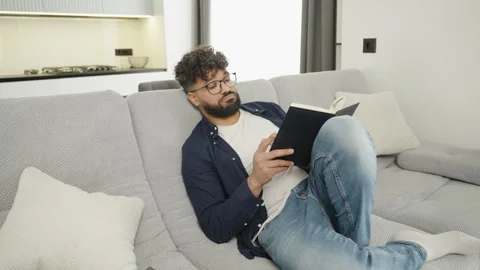 Caucasian man reading book alone at home Video stock 333982041