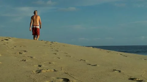 Caucasian man in red swim shorts walking  on the beach Stock Footage