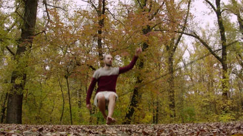 Caucasian man sets slackline between trees in the autumn forest. 스톡 동영상 142093719