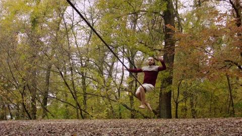 Caucasian man sets slackline between trees in the autumn forest. 스톡 동영상 142093843