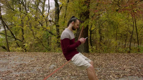 Caucasian man sets slackline between trees in the autumn forest. 스톡 동영상 142116260