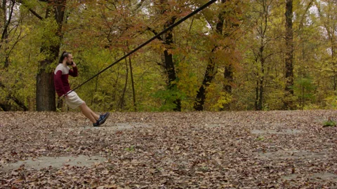 Caucasian man sets slackline between trees in the autumn forest. Vídeo Stock 142116360
