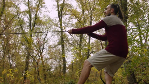Caucasian man sets slackline between trees in the autumn forest. 스톡 동영상 142131787
