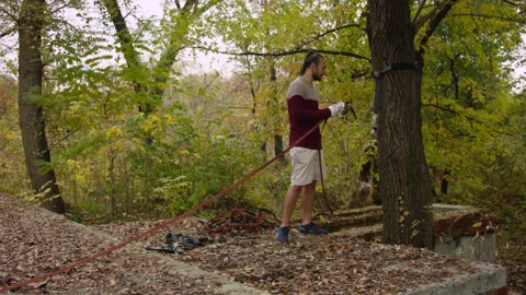 Caucasian man sets slackline between trees in the autumn forest. 스톡 동영상 142253285