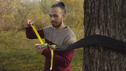 Caucasian man sets slackline between trees in the autumn forest. 스톡 동영상 142301212