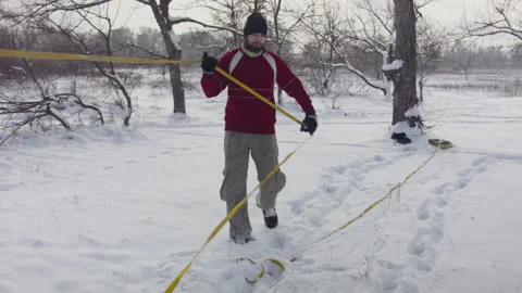 Caucasian man sets slackline between trees in the winter forest. 스톡 동영상 146914983